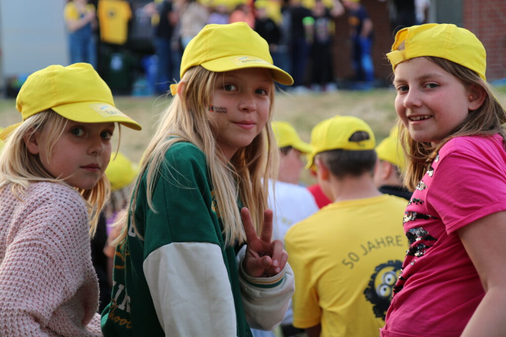 Drei Mädchen mit gelben Kappen, im Hintergrund weitere Kinder