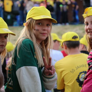 Drei Mädchen mit gelben Kappen, im Hintergrund weitere Kinder