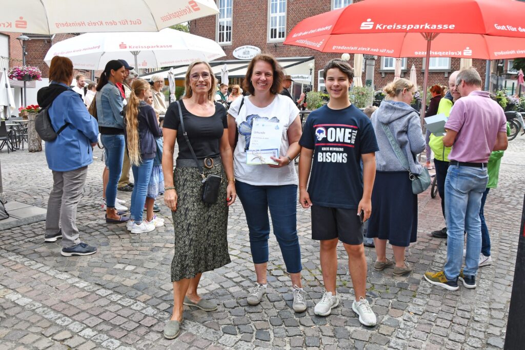 Anja Küppers, Iris Jansen und Erik Braun mit der Urkunde und den gewonnenen Konzerttickets auf dem Roßtorplatz in Wassenberg