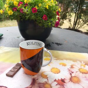 Kolping-Tasse mit Schokolade, dahinter Blumen
